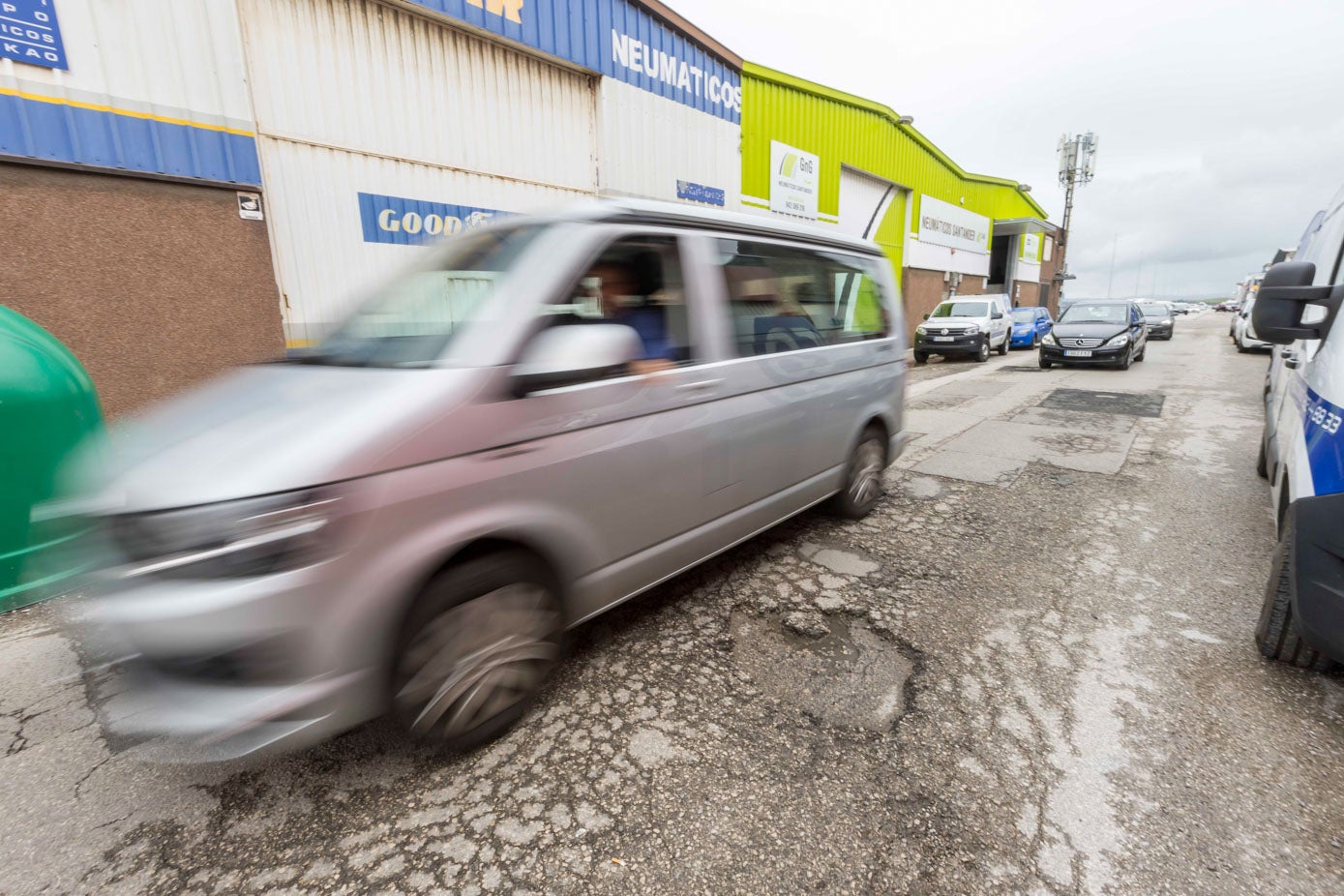 Un vial lleno de baches junto a dos talleres de neumáticos. 