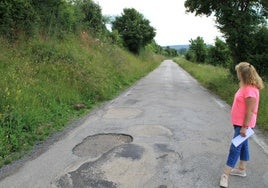 La alcaldesa pedánea de Espinosa de Bricia, Azucena Vallejo, contempla el mal estado en el que se encuentra la carretera. Cartel del límite con Cantabria, hasta donde se completa el desbroce.