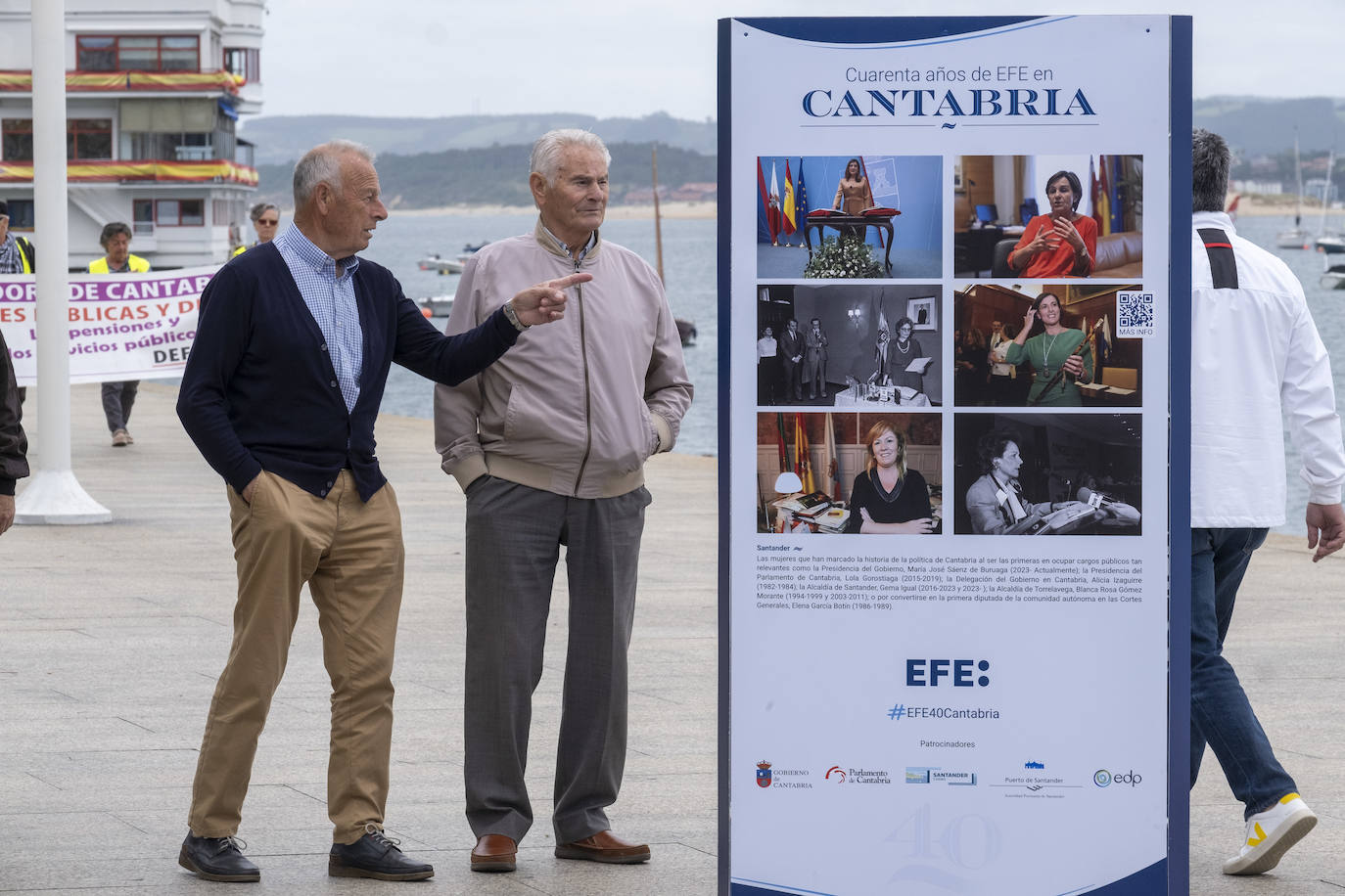 Varios paseantes observan la muestra de fotografías que se encuentra en el muelle Calderón, en Santander. 