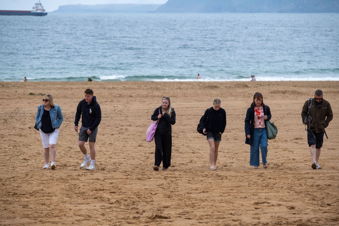 En primer plano, paseantes, y al fondo algunos valientes que se vayan a pesr de la falta de sol