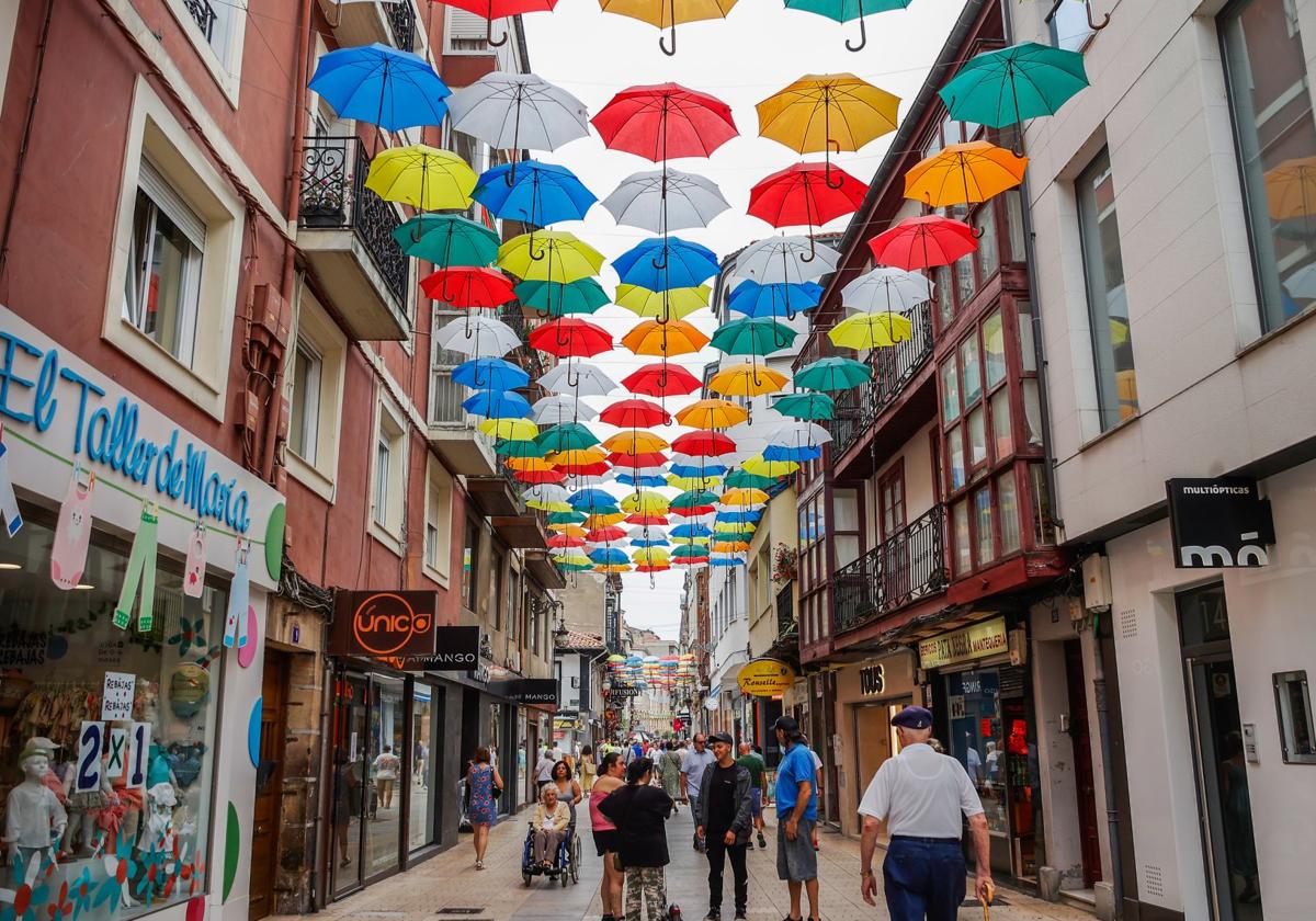 Vecinos caminan por la calle Consolación de Torrelavega, decorada con 900 paraguas de colores durante las fiestas.