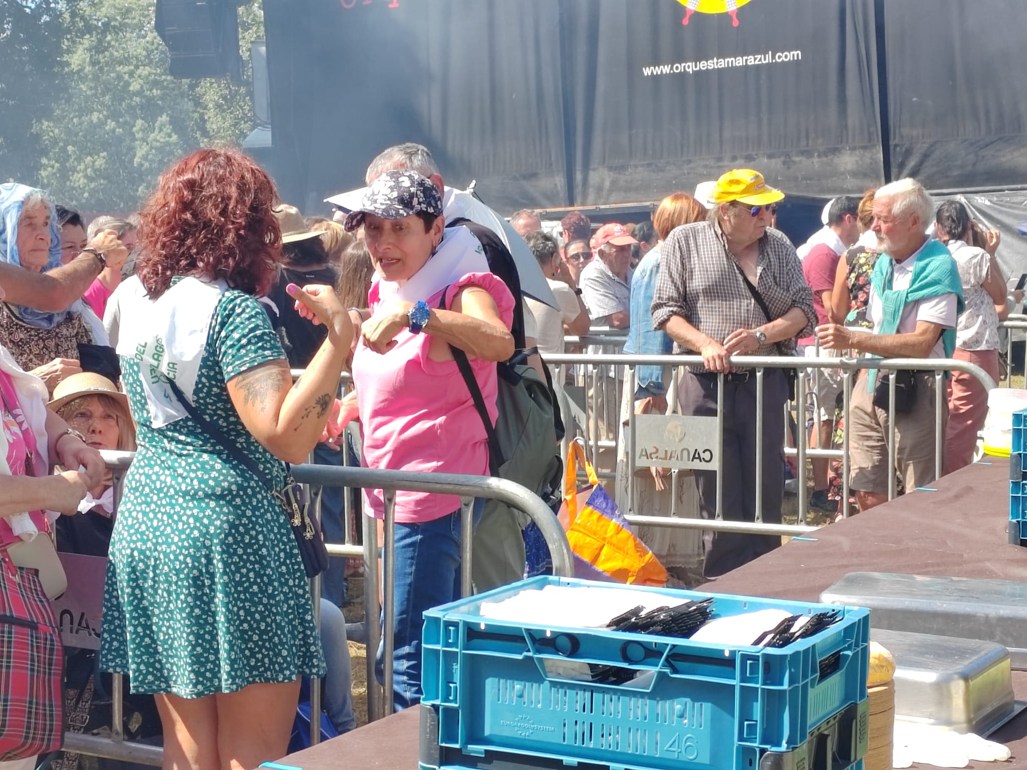 Gorras, paraguas y mangas cortas para protegerse del sol durante la espera para recoger las raciones de paella