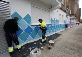 Dos trabajadores pintan un mural en un local municipal de Nueva Ciudad.