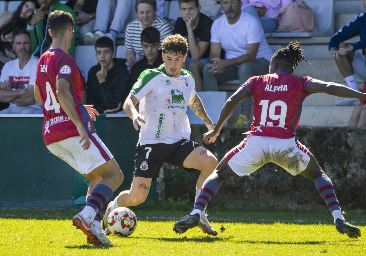 Izan, del Rayo Cantabria, protege el balón ante dos rivales del Ávila