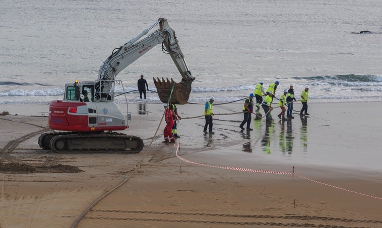 Los operarios llevan a cabo el desembarco del cable submarino de Meta en la playa de la Virgen del Mar (Santander).