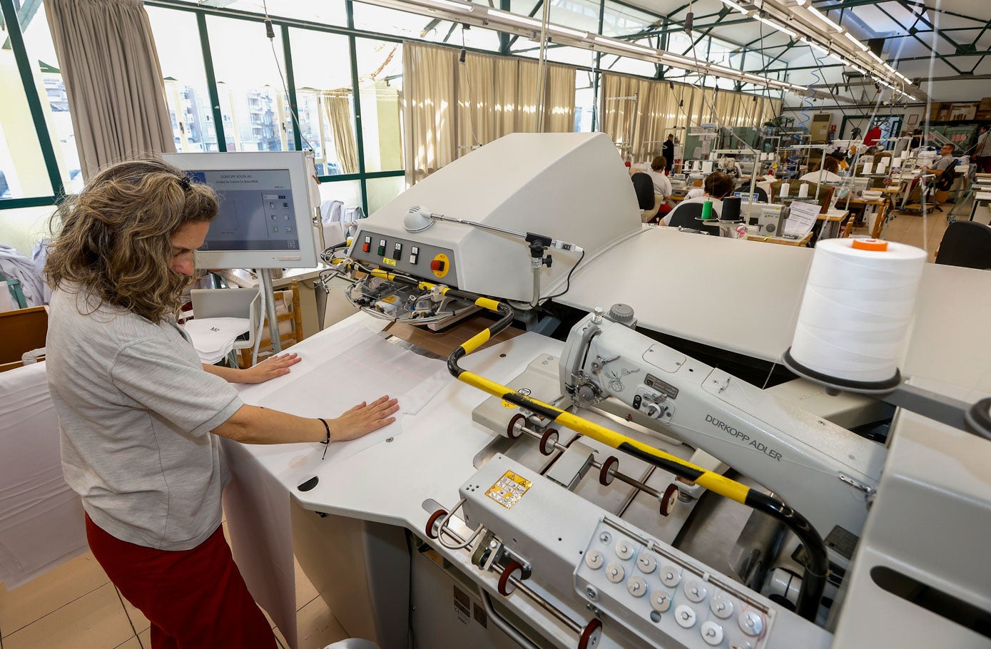 Marisol Calvo cose unos bolsillos en una prenda, con ayuda de una máquina, en el taller de confección. 