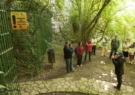 Unos visitantes y una guía junto a la puerta que da acceso a la cueva del Pendo.