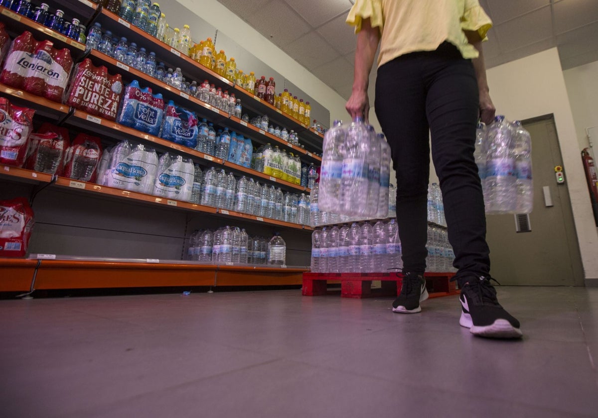 Una persona carga con varias botellas de agua en un supermercado.