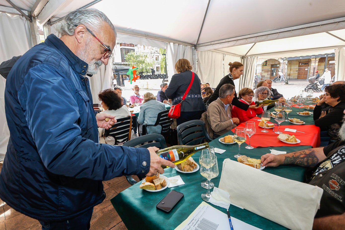 El ﻿profesor y jefe de sala del Hotel Escuela Las Carolinas, Alfonso Fraile, sirve un poco de vino a uno de los vecinos participantes, este lunes, en la plaza Baldomero Iglesias de Torrelavega. 