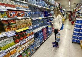 Una mujer coge agua de un estante en un supermercado de Santander.