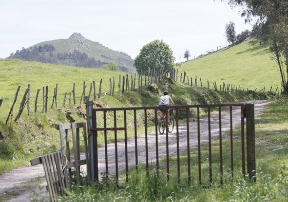 Un ciclista circula por un camino de la sierra del Dobra con el pico La Capía al fondo.