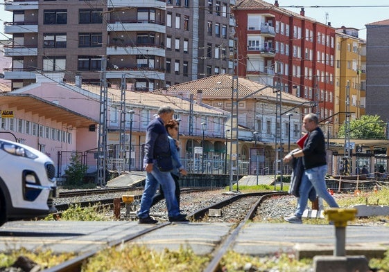 Varios ciudadanos cruzan las vías con la estación al fondo.