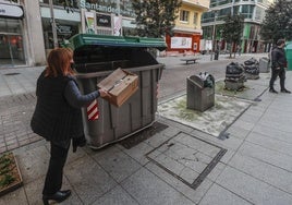 Una vecina de Santander tira basura a un contenedor de la calle Juan de Herrera, con los depósitos de recogida neumática cercanos clausurados.