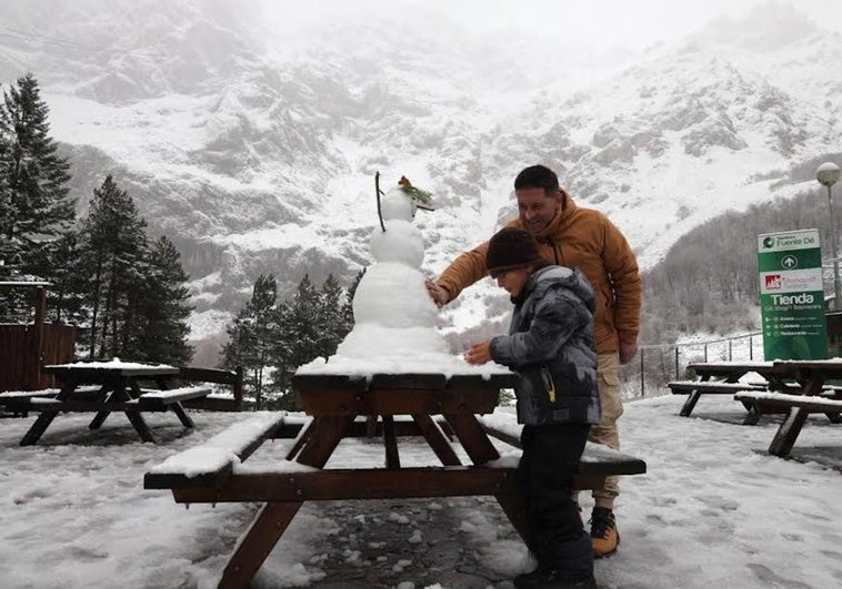 Un niño y su padre hacen un muñeco de nieve en Fuente Dé.