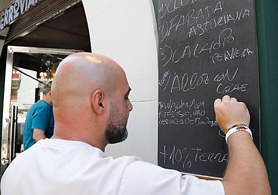 Un camarero escribe en una pizarra el menú del día.