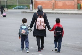 Una mujer extranjera acompaña de la mano a dos niños al colegio.