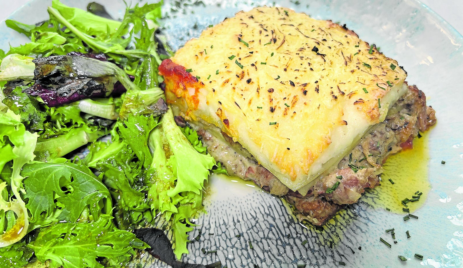 Lasaña de carne con bechamel sobre fondo de tomate y gratinada al horno.