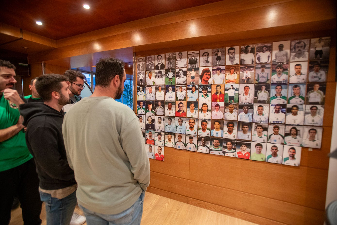 Varios asistentes observan un panel de fotografías con jugadores que han sido internacionales.