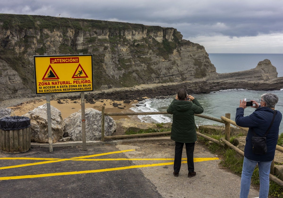 Dos personas realizan ayer una fotografía en la playa pequeña de Langre. A su lado, el cartel donde se prohíbe el acceso.