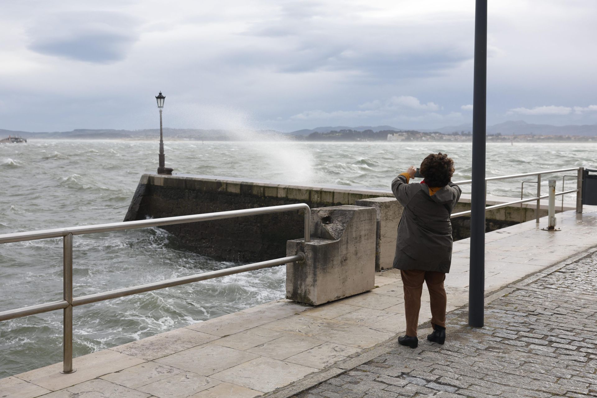 Una mujer fotografía las olas en el paseo marítimo de Santander