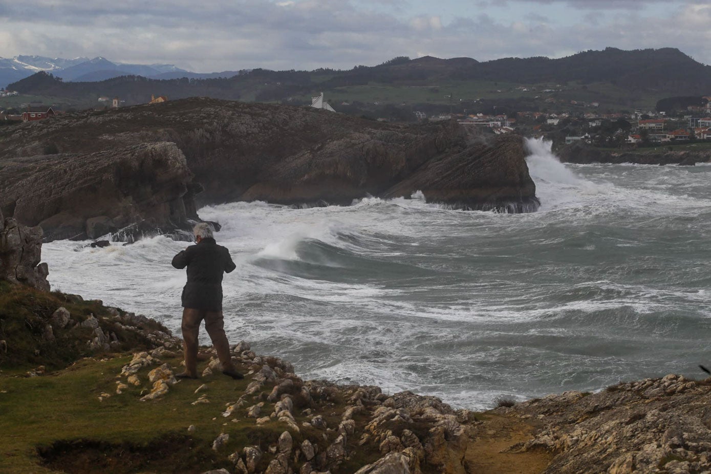 Un hombre fotografía el mar desde lo alto de un acantilado.