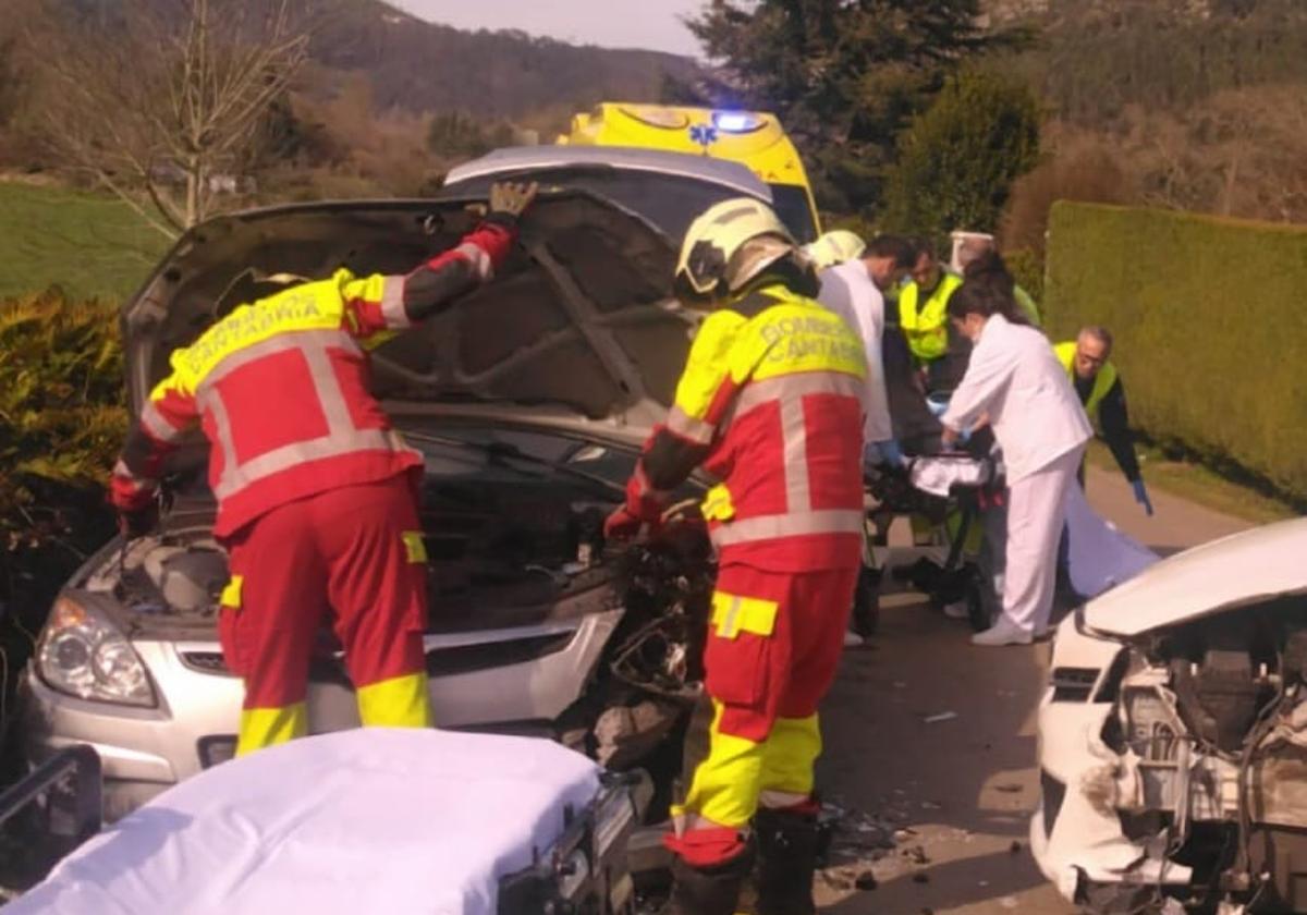 Los servicios sanitarios atienden a uno de los heridos mientras los bomberos revisan uno de los turismo implicados.