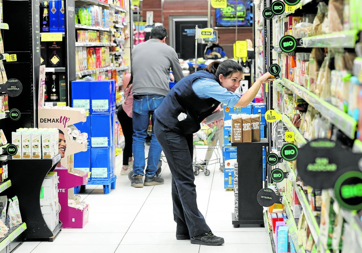 Una reponedora coloca productos en las baldas de un pasillo de un supermercado.