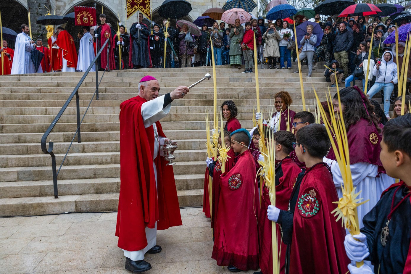 El Obispo de Santander, Arturo Ros, bendice las palmas a los pies de la catedral bajo la lluvia fina.