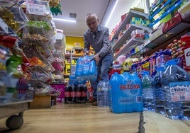 Aixiong Ye reponiendo botellas y garrafas de agua en su tienda.