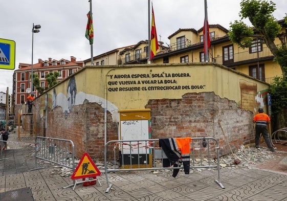 Un vecino camina frente al mural de la Peña Bolística de Torrelavega mientras los operarios trabajan en las labores de picado.