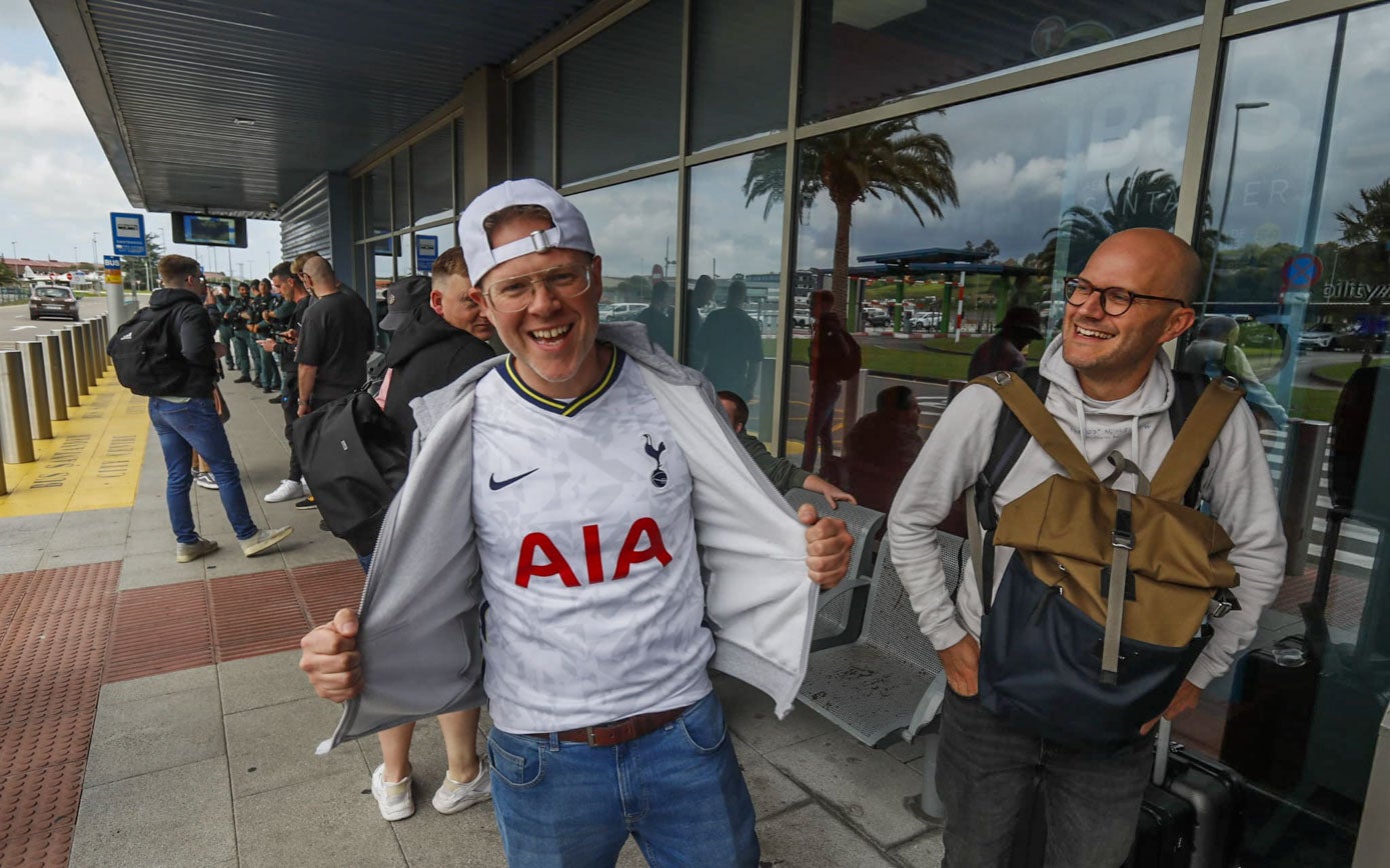 Un seguidor del Tottenham ríe mientras enseña su camiseta en el aeropuerto.