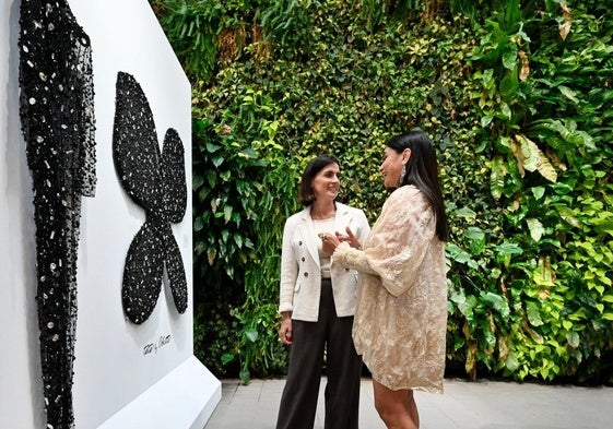 Odette Álvarez explica a la alcaldesa de Santander que con el vestido negro de abalorios expuesto en la pared, acompañado de unas alas confeccionadas en colaboración con Farid Joyeros, desfiló por primera vez en la Mercedes-Benz Fashion Week Madrid.