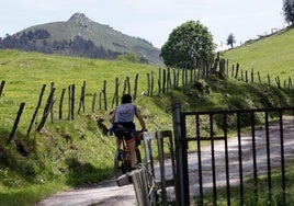 Un ciclista circula por le Monte Dobra con el pico de La Capía al fondo.