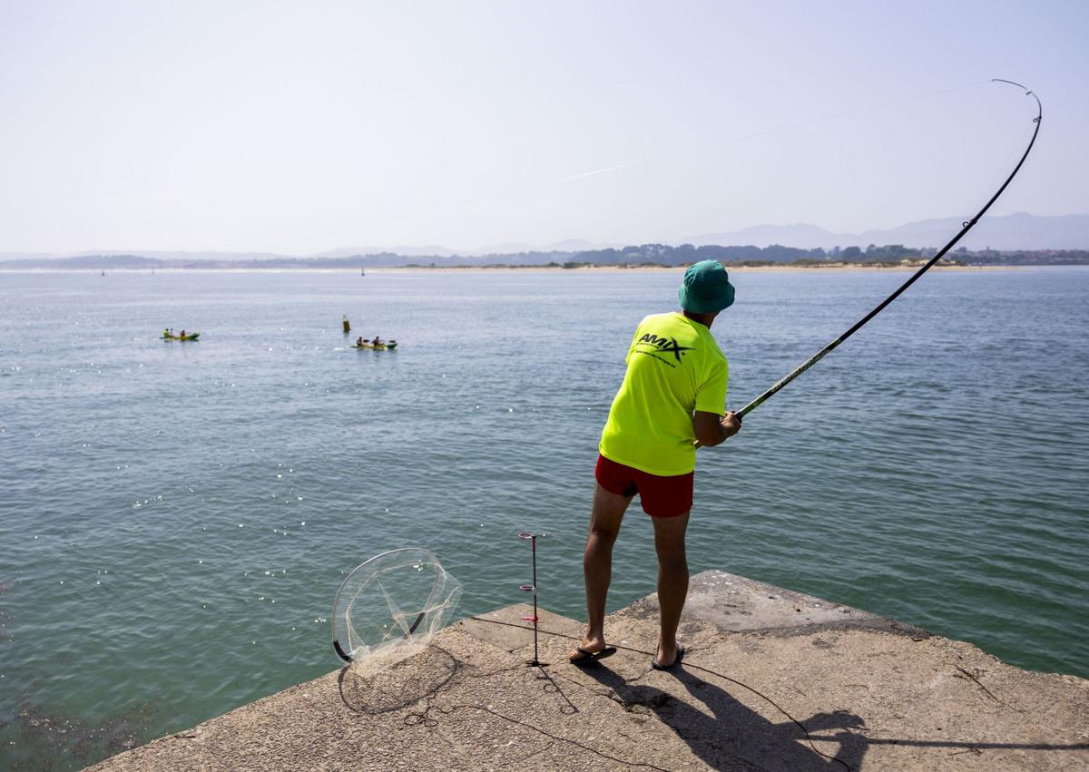 Imagen secundaria 1 - A la izquierda, un pescador lanza su caña al lado de la playa de Los Peligros. A la derecha, un pescador, sentado en un noray junto al mar. 