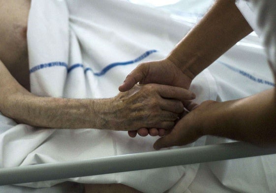 Un paciente agarra su mano a la de un profesional que le atiende al final de su vida.