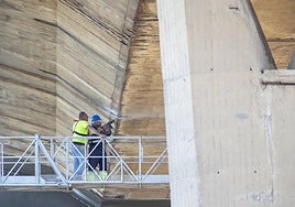 Dos operarios trabajan en la parte inferior del puente para renovar el hormigón y la estructura metálica.