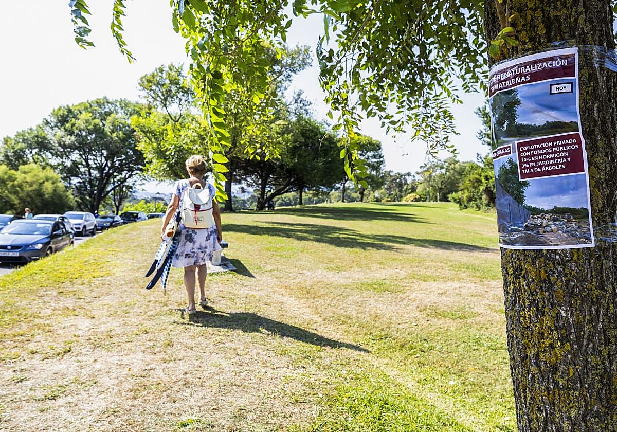 Una mujer pasea por la zona donde se desarrollará el aparcamiento y un árbol recoge las protestas de los vecinos de Cueto.