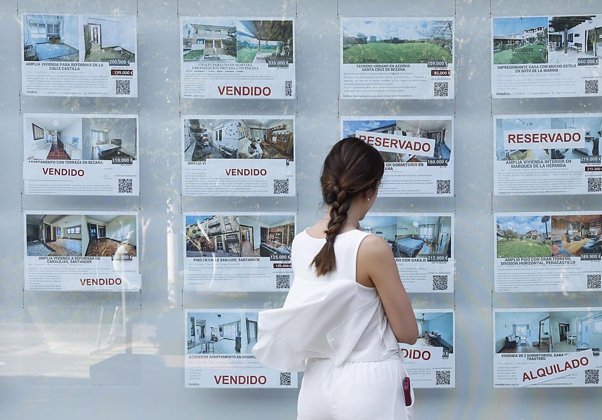 Una mujer mira anuncios de venta de viviendas en el escaparate de una agencia inmobiliaria.