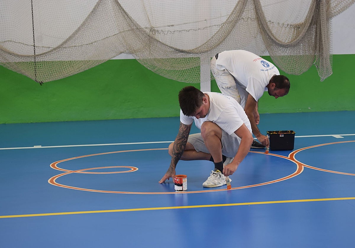 Operarios realizan labores de mantenimiento en la pista del polideportivo.