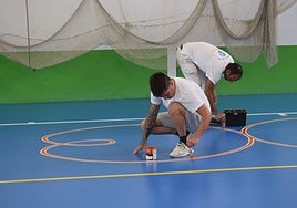 Operarios realizan labores de mantenimiento en la pista del polideportivo.
