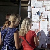 Jóvenes comprueban anuncios de alquiler en un tablón.