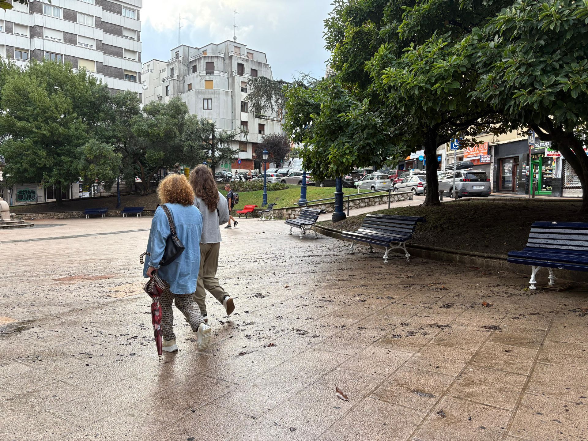 Dos mujeres pasean, paragüas en mano, por el centro de Santander. Después de la tromba de agua ha salido el sol.