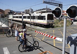 Un tren parte de la estación de Torrelavega mientras vecinos esperan en el paso a nivel de Pablo Garnica, en Torrelavega.