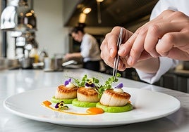 Con ayuda de unas pinzas un chef coloca brotes y pétalos sobre unas vieiras marcadas a la plancha y emplatadas sobre un puré de aguacate.