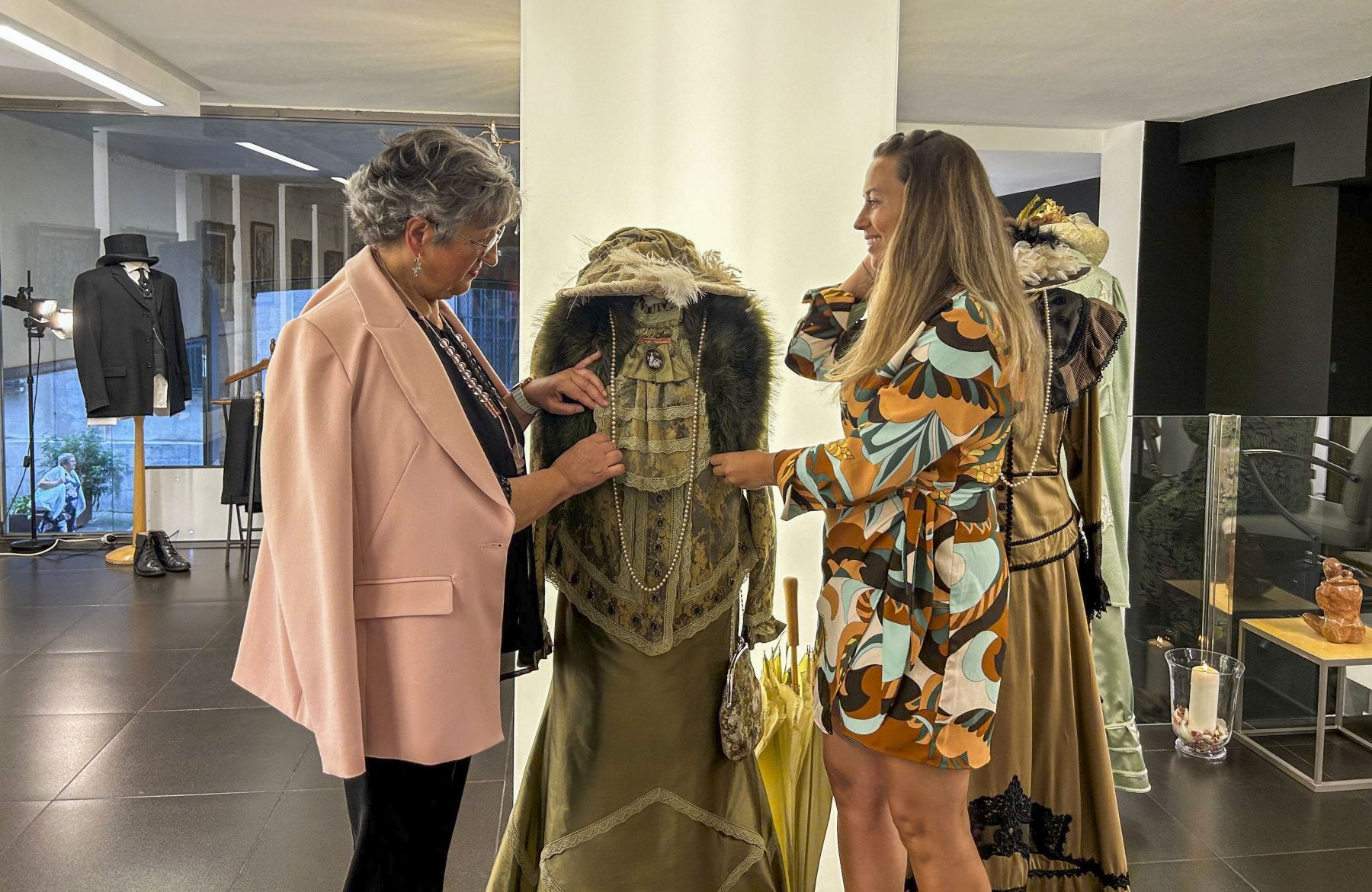 María José Mínguez y su hija, Irene Coté, junto a uno de los trajes de la exposición que se puede contemplar en el Pasaje de Saro de Torrelavega.