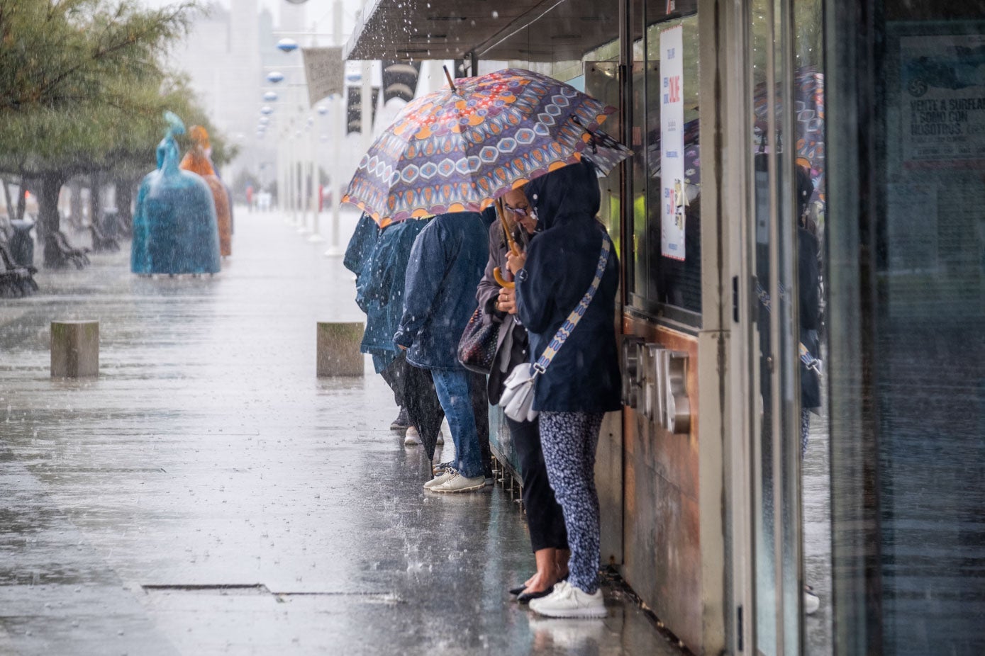 Unos turistas se guarecen del agua en la estación de las lanchas a Pedreña.