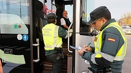 Dos agentes de la Guardia Civil inspeccionan un vehículo de tranpsorte escolar.