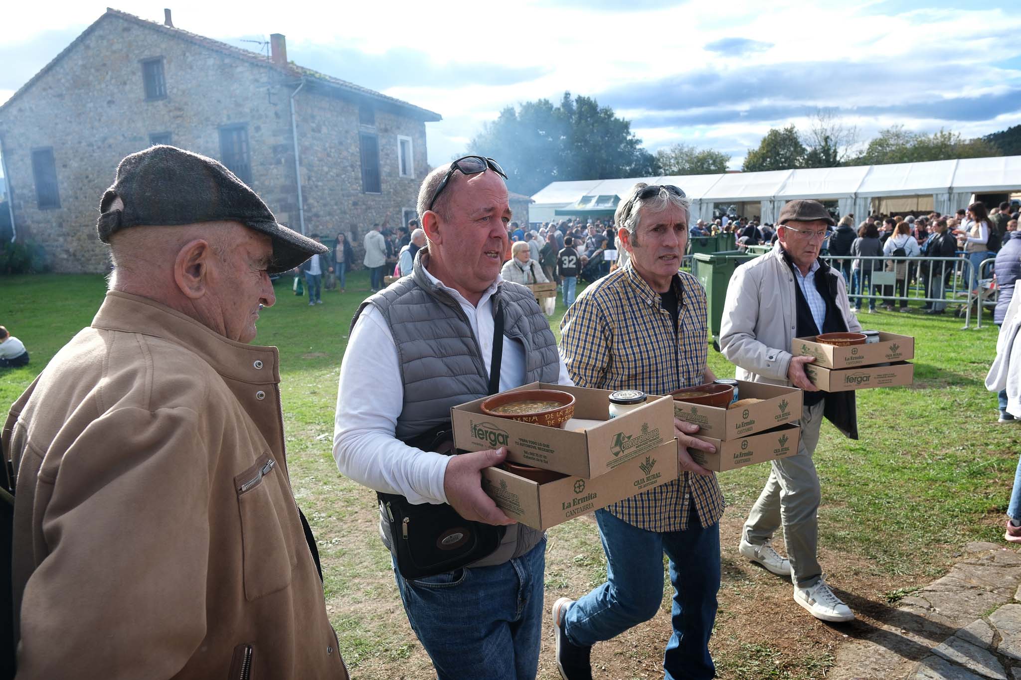 Asistentes a la feria cargan con varias raciones de cocido montañés todavía caliente. 