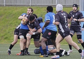 Un jugador intentando ganar metros con el balón mientras el rival trata de placarlo.
