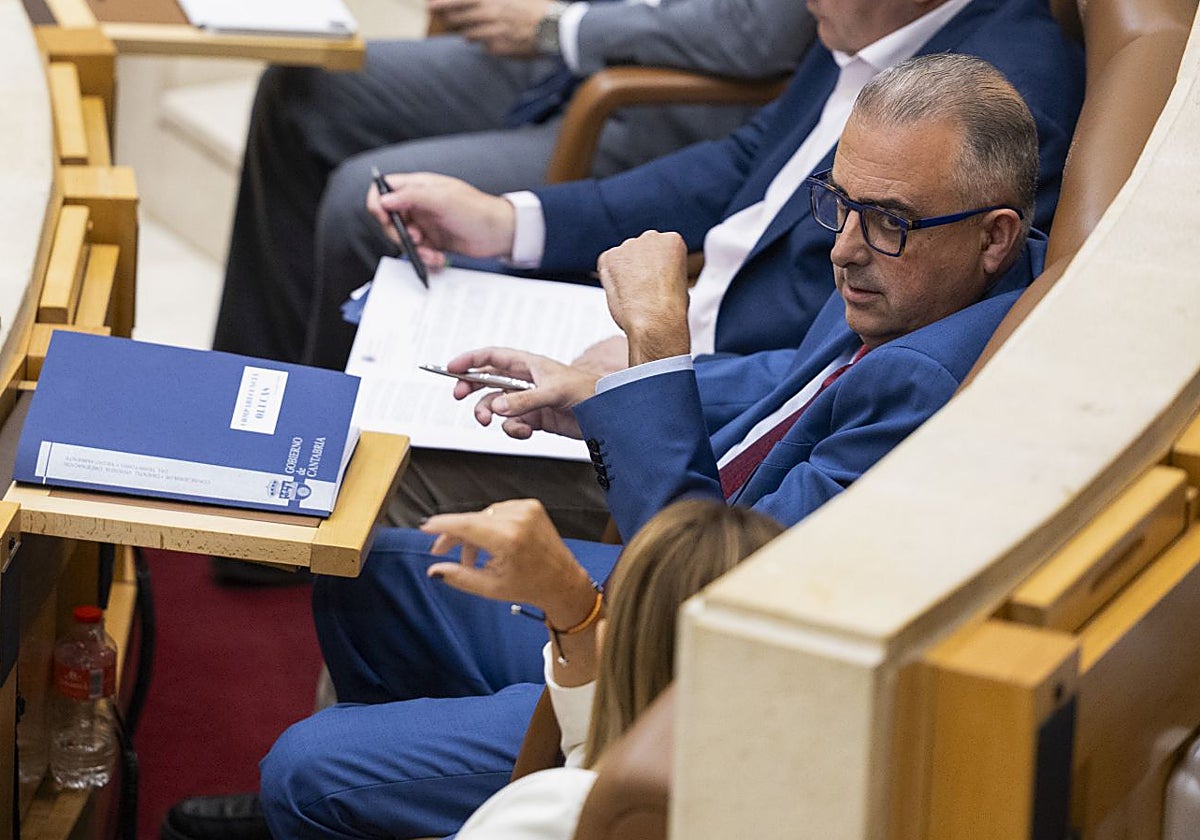El consejero Media charla con la presidenta Buruaga (de espaldas), durante el pleno en el Parlamento regional.